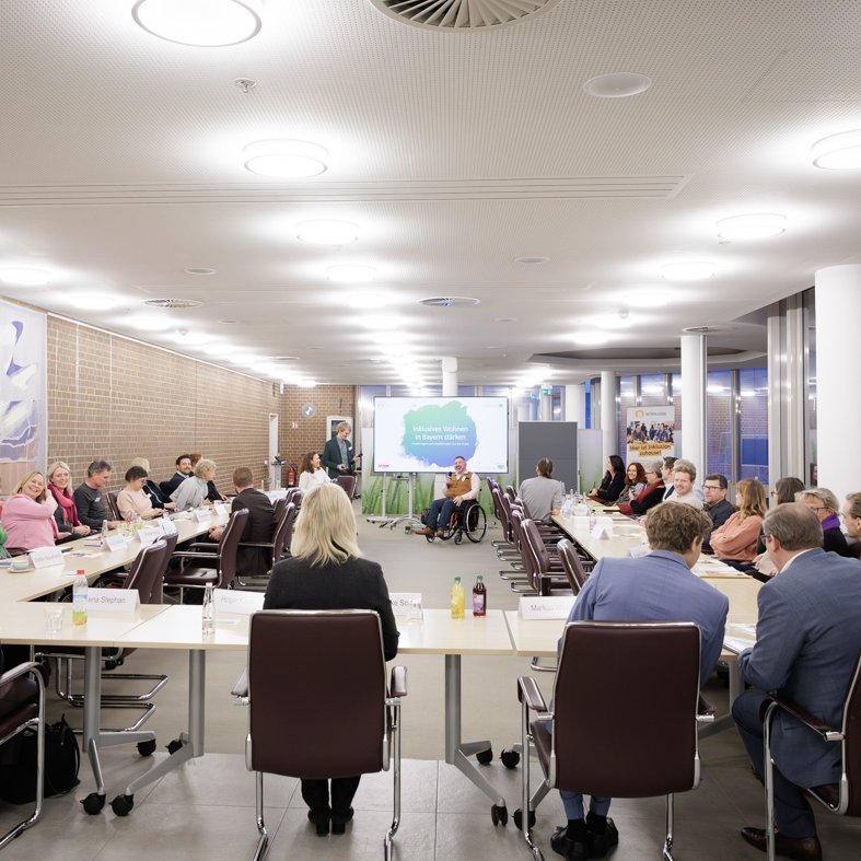 In einem Konferenzraum sitzen ca. 30 Personen in U-Form. Mittig sitzt Sozialministerin Ulrike Scharf. Vorne präsentieren Holger Kiesel und Tobias Polsfuß.