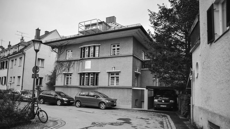 Außenansicht der Villa mmhh. Ein zweistöckiges Mehrfamilienhaus in einer ruhigen Straße. Foto in Schwarz-Weiß.