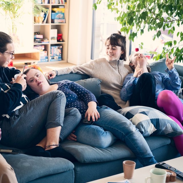 5 Mitbewohner einer inklusiven WG sitzen gemeinsam auf der Couch und albern herum