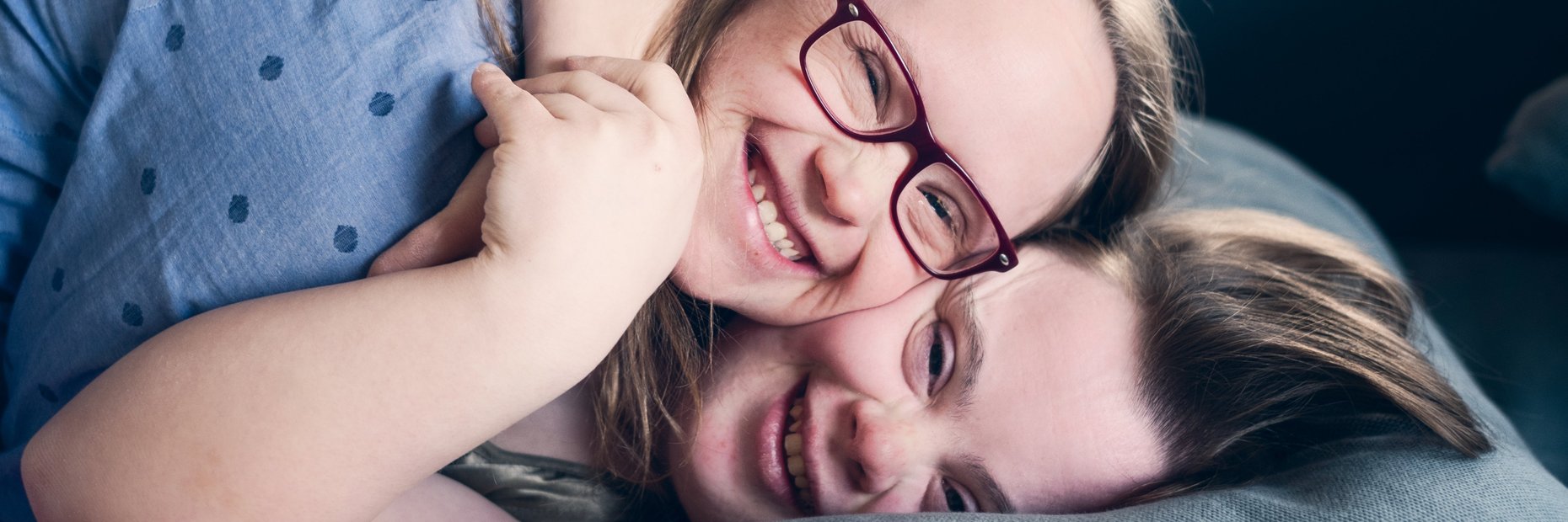 Zwei Mitbewohnerinnen mit Downsyndrom einer inklusiven WG liegen freundschaftlich umschlungen auf der Couch und kuscheln