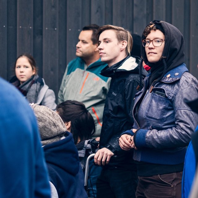 Eine Gruppe Menschen steht im Freien vor dem "Blauhaus" Bremen und hört jemandem zu. Es ist kalt, sie tragen Regenkleidung.