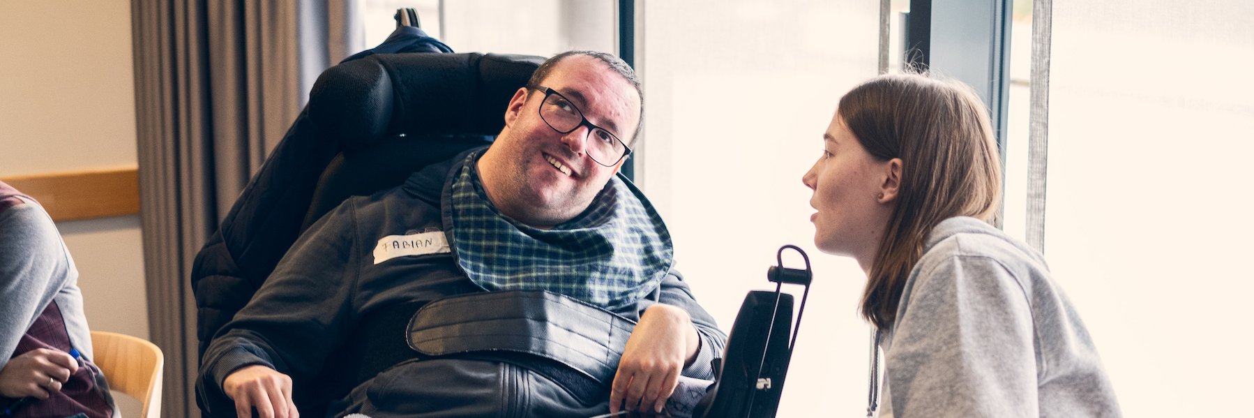 Eine junger Mann im E-Rollstuhl unterhält sich mit einer jungen Frau
