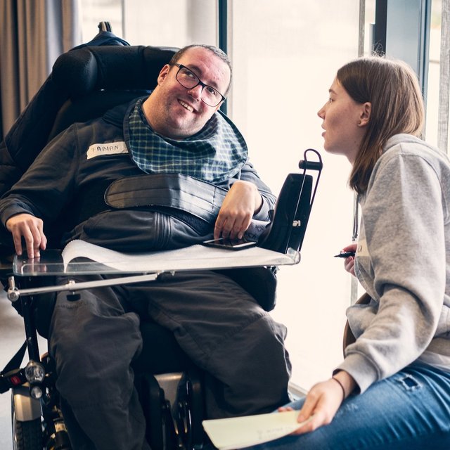 Eine junger Mann im E-Rollstuhl unterhält sich mit einer jungen Frau