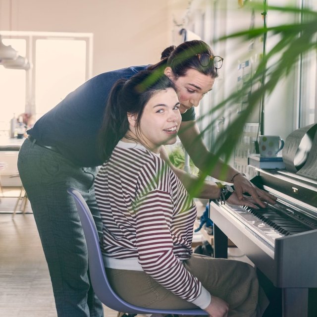 Eine Mitbewohnerin mit Behinderung und ein Mitbewohner ohne Behinderung sitzen gemeinsam am Klavier und spielen